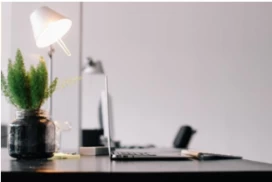 A desk with a computer, lamp, and plant