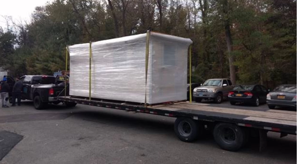  A small prefabricated building wrapped up on a flatbed trailer.