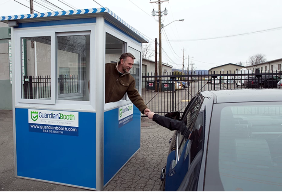 Man in a blue parking booth helping a customer in a car