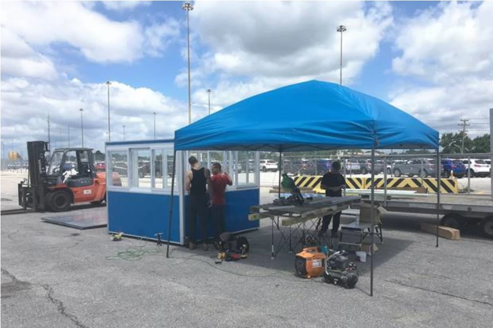 Workers assembling a blue guard booth in a parking lot.