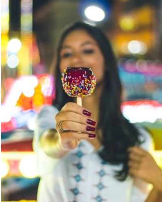 A girl holding a sprinkle coated candy apple at an affair. 