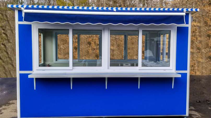 A-blue-prefabricated-booth-featuring-large-sliding-windows-and-a-striped-roll-up-awning